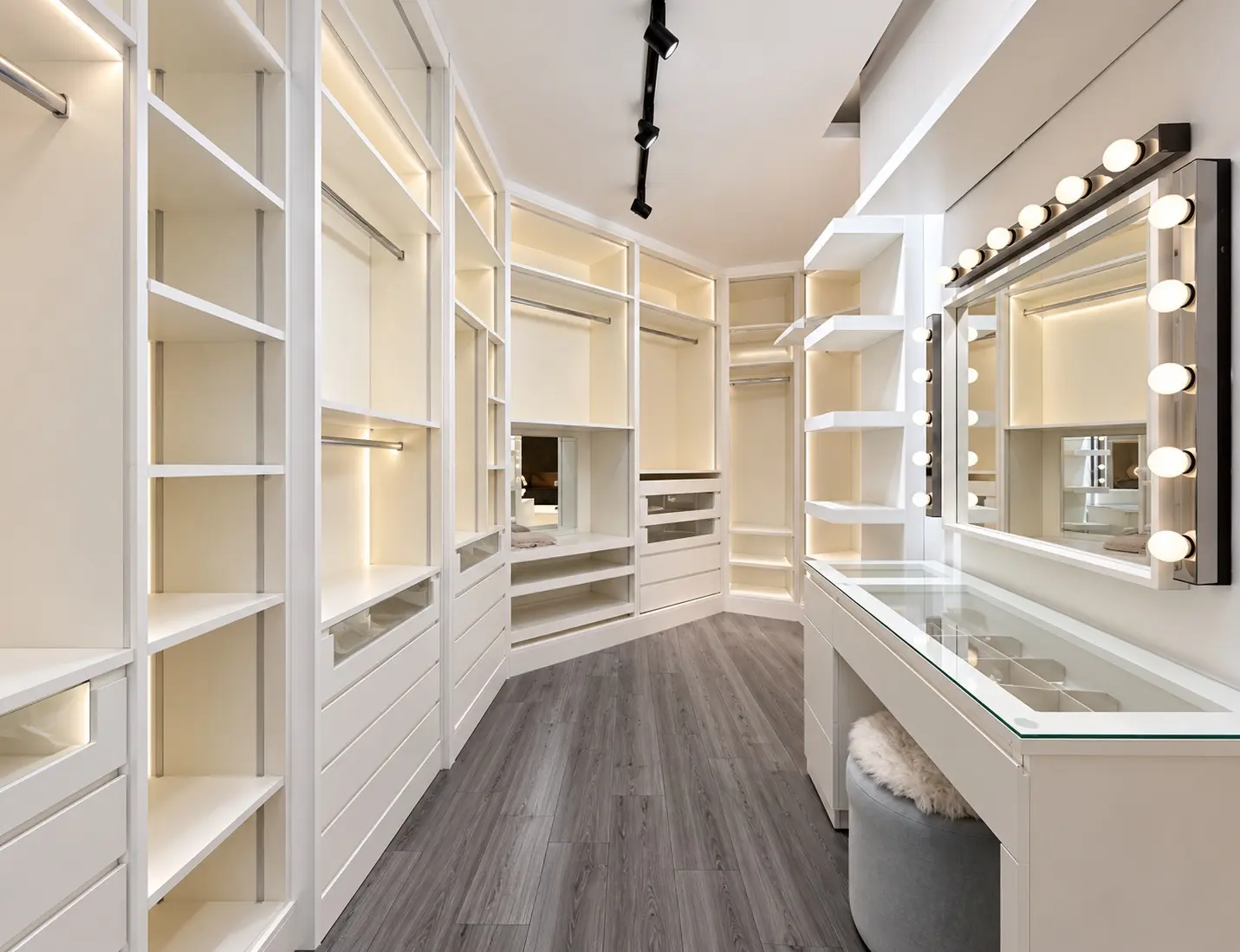Renovated white walk-in wardrobe with illuminated shelving and dressing table